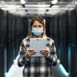 Female informatic engineer working inside server room database while wearing face mask