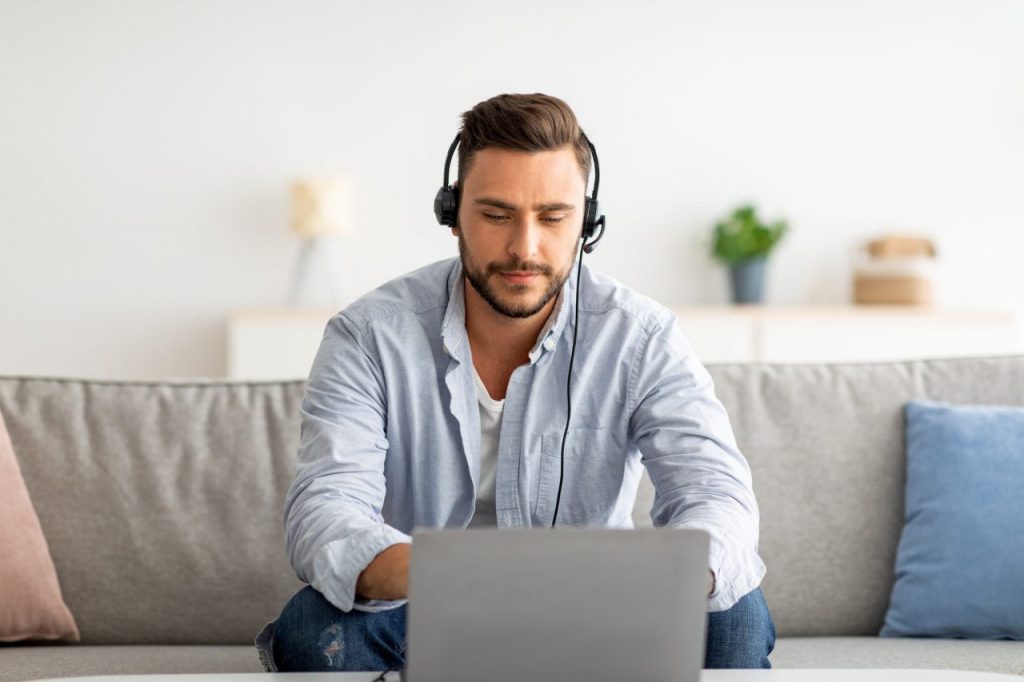 Hotline support service Millennial male call center operator in headset working with laptop at home