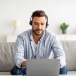 Hotline support service Millennial male call center operator in headset working with laptop at home